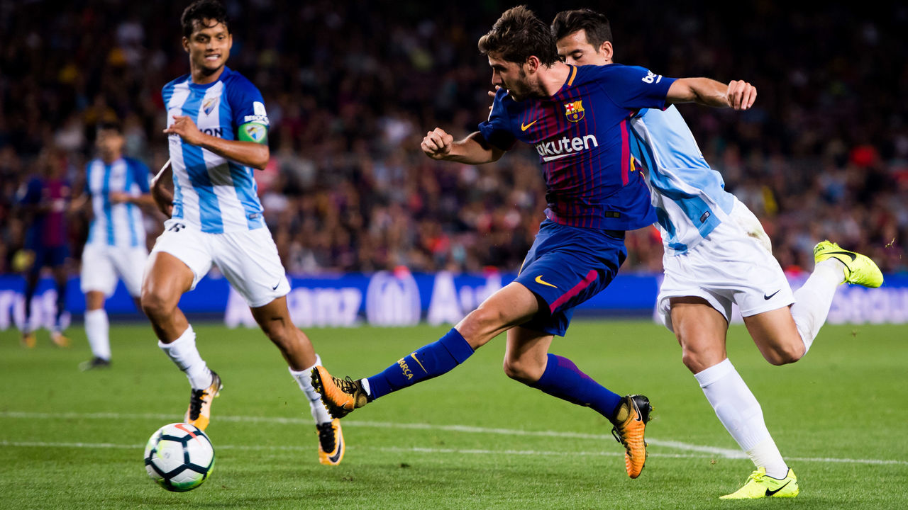 BARCELONA, SPAIN - OCTOBER 21: Sergi Roberto of FC Barcelona shoots the ball under pressure from Luis Hernandez of Malaga CF during the La Liga match between Barcelona and Malaga at Camp Nou on October 21, 2017 in Barcelona, Spain.