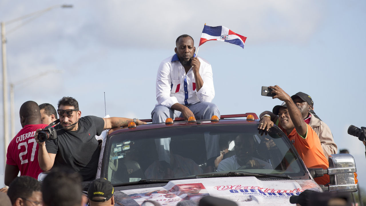 Former Dominican Major League baseball player Vladimir Guerrero (C) holds a Dominican flag as he is driven through the streets after arriving at the Las Americas Airport in Santo Domingo, Dominican Republic on January 28, 2018. Guerrero, who was elected to the Baseball Hall of Fame this week, was welcomed with honors by the country's sports and tourism ministers. / AFP PHOTO / Erika SANTELICES