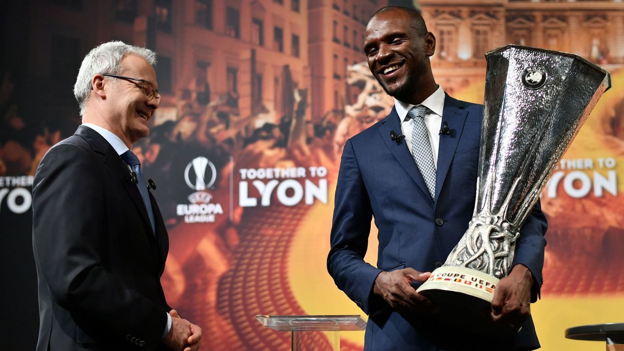 UEFA Deputy General Secretary Giorgio Marchetti Giorgio Marchetti (L) and former French football player and ambassador for the UEFA Europa League final in Lyon, Eric Abidal share a light moment during the hand over of the trophy after the draw for the semi-finals round of the UEFA Europa League football tournament at the UEFA headquarters in Nyon on April 13, 2018. / AFP PHOTO / Fabrice COFFRINI