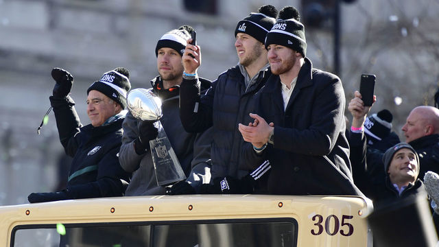 PHILADELPHIA, PA - FEBRUARY 08: (L-R) Team owner Jeffrey Lurie, with quarterbacks Nick Foles #9, Nate Sudfeld #7 and Carson Wentz #11 of the Philadelphia Eagles, acknowledge fans as Foles holds the Vince Lombardi Trophy atop a parade bus during festivities on February 8, 2018 in Philadelphia, Pennsylvania. The city celebrated the Philadelphia Eagles' Super Bowl LII championship with a victory parade.