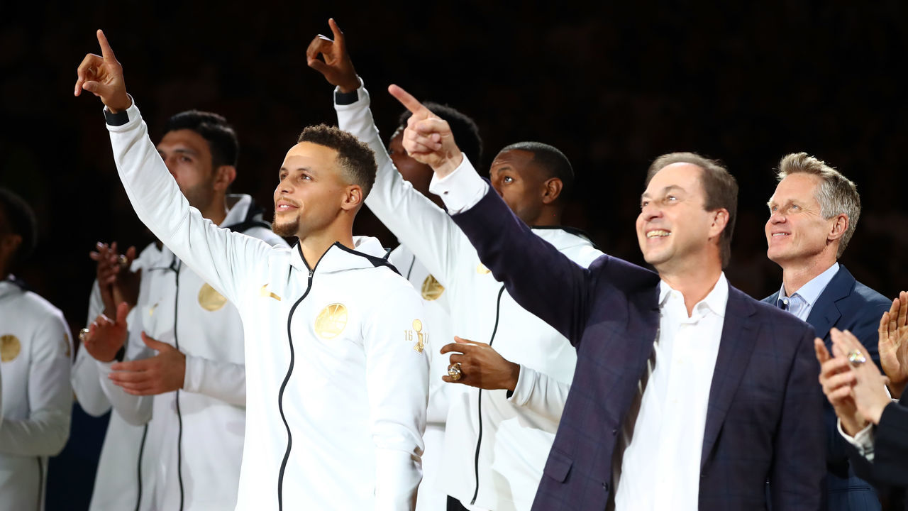 OAKLAND, CA - OCTOBER 17: Stephen Curry #30, owner Joe Lacob and the Golden State Warriors point to their 2017 NBA Championship banner prior to their NBA game against the Houston Rockets at ORACLE Arena on October 17, 2017 in Oakland, California.