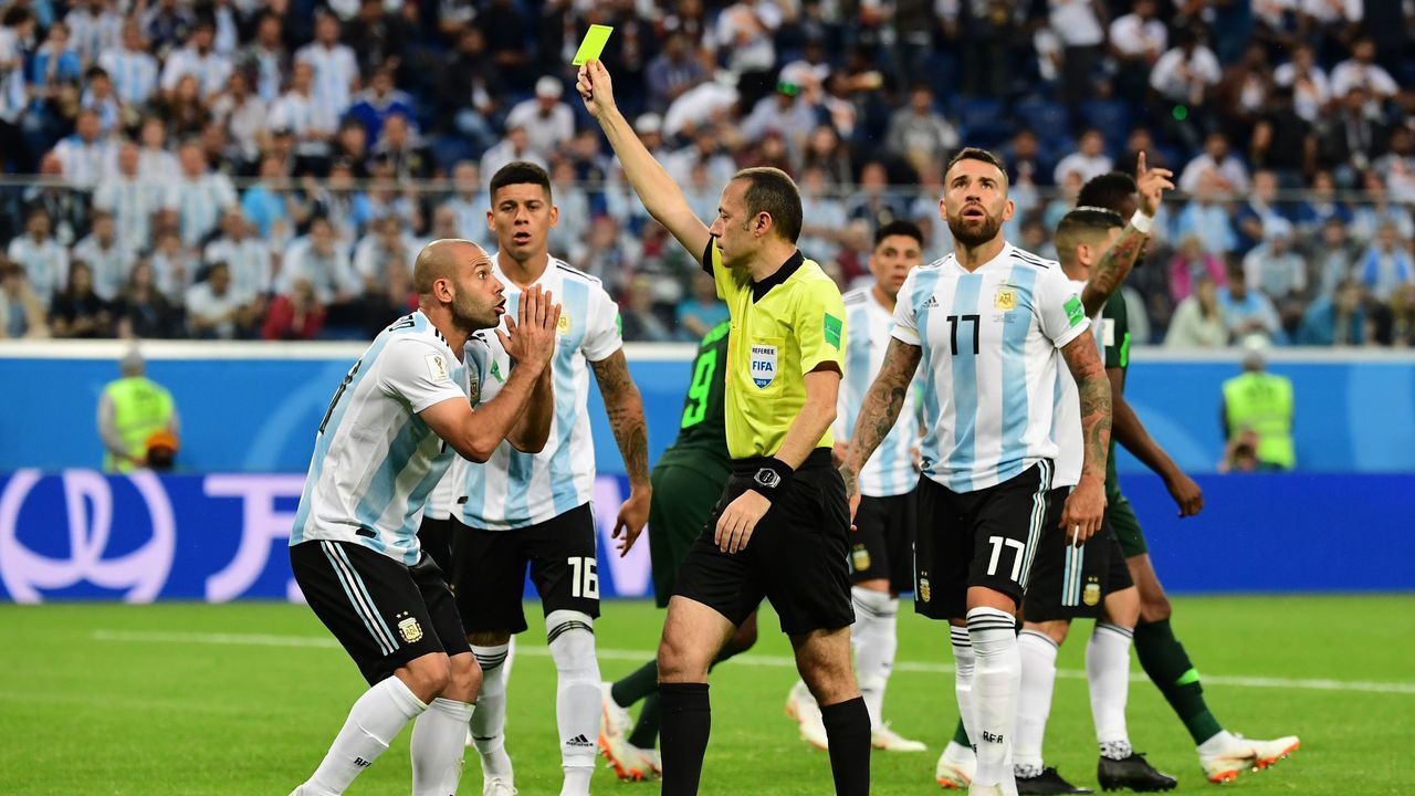 Turkish referee Cuneyt Cakir (C) presents Argentina's midfielder Javier Mascherano (L) with a yellow card during the Russia 2018 World Cup Group D football match between Nigeria and Argentina at the Saint Petersburg Stadium in Saint Petersburg on June 26, 2018.