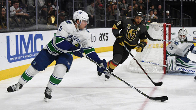 LAS VEGAS, NV - MARCH 20: Derrick Pouliot #5 of the Vancouver Canucks skates with the puck against Pierre-Edouard Bellemare #41 of the Vegas Golden Knights as Jacob Markstrom #25 of the Canucks tends net in the second period of their game at T-Mobile Arena on March 20, 2018 in Las Vegas, Nevada. The Golden Knights won 4-1.