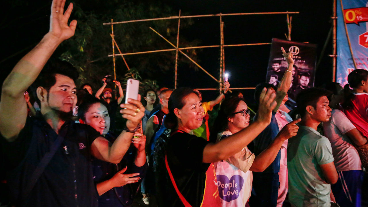 CHIANG RAI, THAILAND - JULY 9: Onlookers watch and cheer as ambulances transport some of the rescued schoolboys from a helipad to a hospital on July 9, 2018 in Chiang Rai, Thailand. Divers began an effort to pull the 12 boys and their soccer coach on Sunday morning after they were found alive in the cave at northern Thailand. Videos released by the Thai Navy SEAL shows the boys, aged 11 to 16, and their 25-year-old coach are in good health in Tham Luang Nang Non cave and the challenge now will be to extract the remaining party safely.