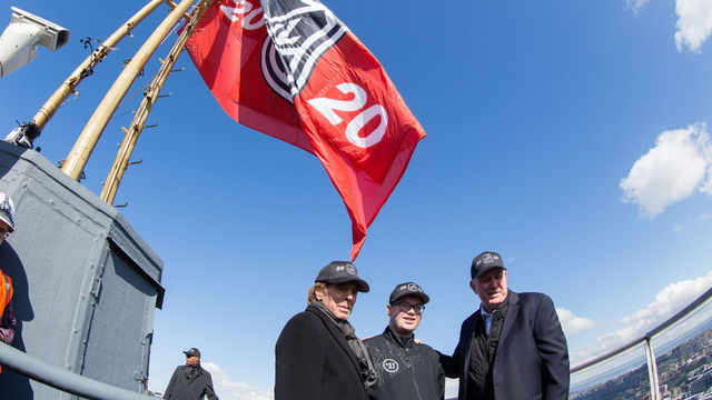 SEATTLE, WA - MARCH 1: Jerry Bruckheimer, honorary captain Bretton Chitwood (17) and Oak View Group Chief Executive Officer Tim Leiweke stand beneath the NHL 2020 flag on the top of the Space Needle during the NHL Seattle season ticket deposit drive kickoff on Thursday, March 1, 2018 in Seattle, WA.