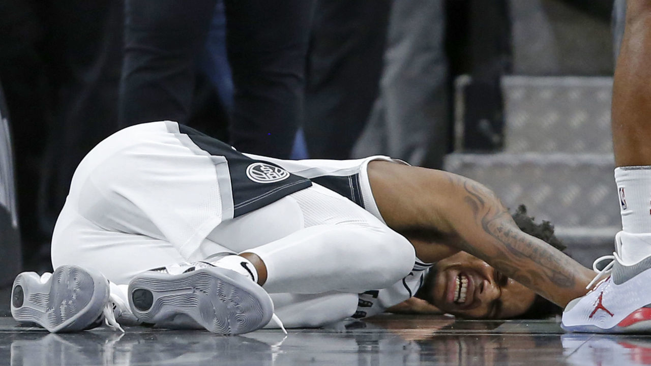 SAN ANTONIO, TX - OCTOBER 7: Dejounte Murray #5 of the San Antonio Spurs reacts after being injured on a play during a preseason game against the Houston Rockets on October 7, 2018 at the AT&T Center in San Antonio, Texas.