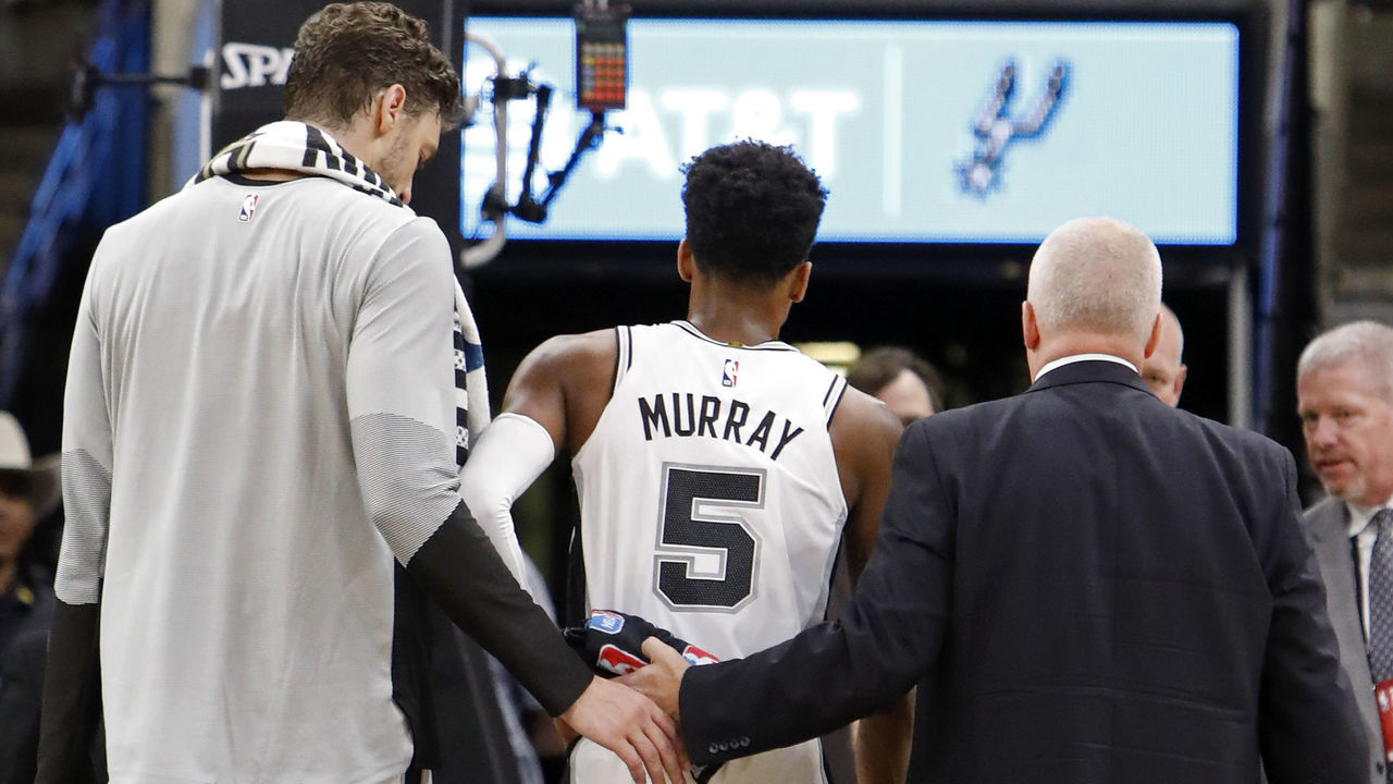 SAN ANTONIO, TX - OCTOBER 7: Dejounte Murray #5 of the San Antonio Spurs walks off the court after being injured on a play as teammate Pau Gasol #16 looks on during a preseason game against the Houston Rockets on October 7, 2018 at the AT&T Center in San Antonio, Texas.