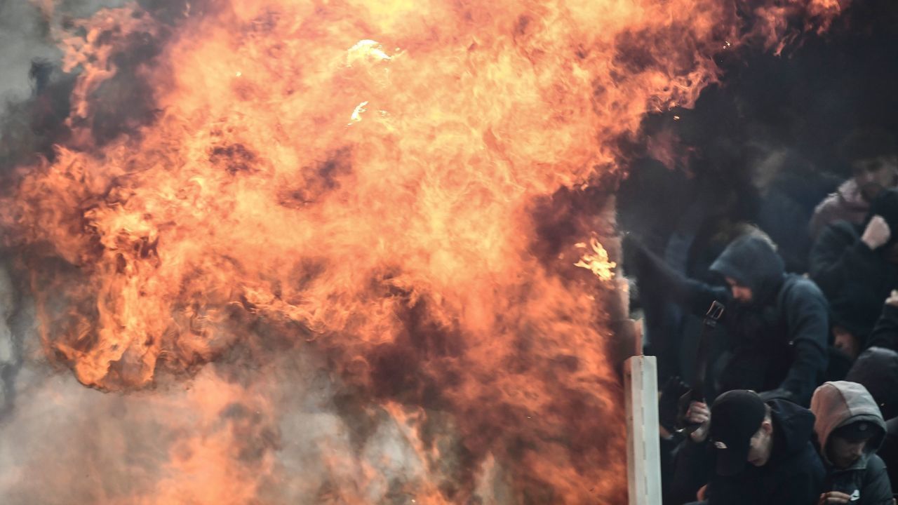 Ajax fans try to shield themselves from flames during clashes with Greek riot police prior to the start of the UEFA Champions League football match between AEK Athens FC and AFC Ajax at the Athens Olympic stadium, in Athens, on November 27, 2018.