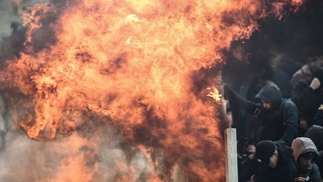 Ajax fans try to shield themselves from flames during clashes with Greek riot police prior to the start of the UEFA Champions League football match between AEK Athens FC and AFC Ajax at the Athens Olympic stadium, in Athens, on November 27, 2018.