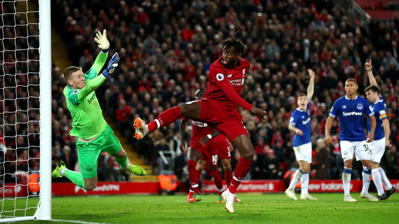 LIVERPOOL, ENGLAND - DECEMBER 02: Divock Origi of Liverpool shoots under pressure from Jordan Pickford of Everton during the Premier League match between Liverpool FC and Everton FC at Anfield on December 2, 2018 in Liverpool, United Kingdom.