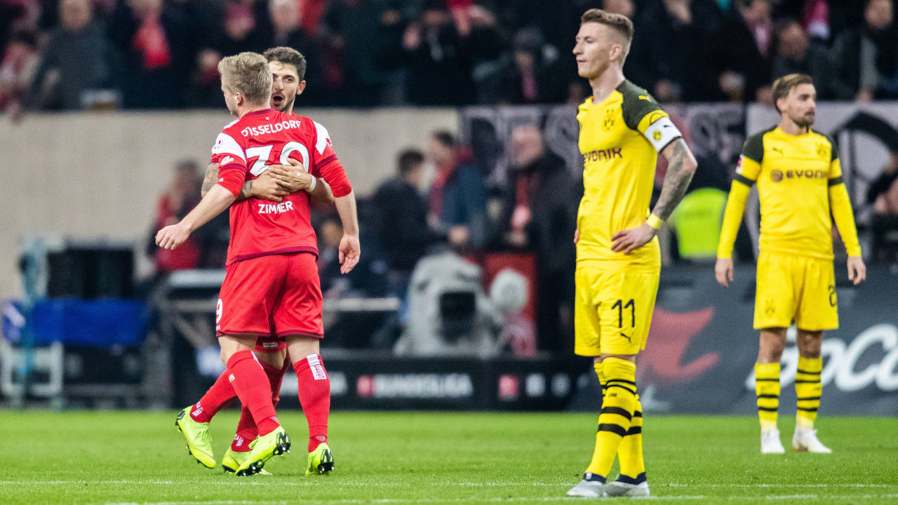 18 December 2018, North Rhine-Westphalia, Düsseldorf: Soccer: Bundesliga, Fortuna Düsseldorf - Borussia Dortmund, 16th matchday in the Merkur Spiel-Arena. Düsseldorf's Matthias Zimmermann (2nd from left) and Düsseldorf's Jean Zimmer (left) are happy after the 2:0. Dortmund's Marco Reus (left) is in front. Photo: Marcel Kusch/dpa - IMPORTANT NOTE: In accordance with the requirements of the DFL Deutsche Fußball Liga or the DFB Deutscher Fußball-Bund, it is prohibited to use or have used photographs taken in the stadium and/or the match in the form of sequence images and/or video-like photo sequences.