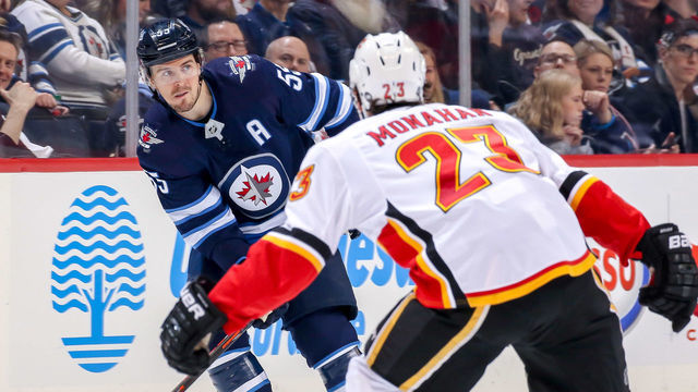 WINNIPEG, MB - DECEMBER 27: Mark Scheifele #55 of the Winnipeg Jets plays the puck down the ice as Sean Monahan #23 of the Calgary Flames defends during second period action at the Bell MTS Place on December 27, 2018 in Winnipeg, Manitoba, Canada.