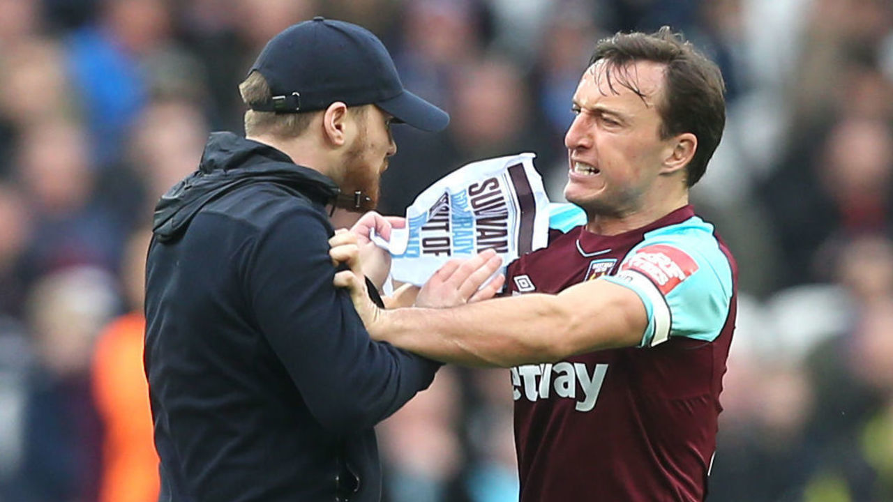 LONDON, ENGLAND - MARCH 10: Mark Noble of West Ham fights with a pitch invader protesting the board of directors during the Premier League match between West Ham United and Burnley at London Stadium on March 10, 2018 in London, England.