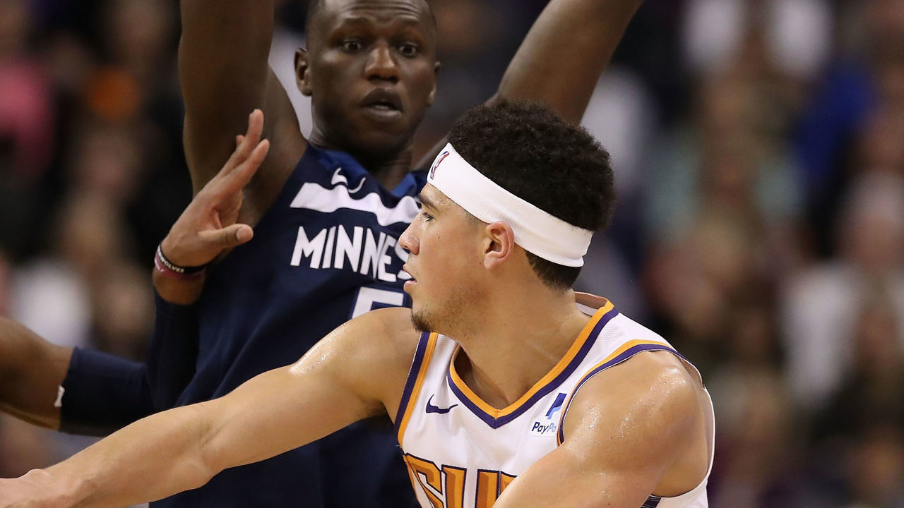 PHOENIX, ARIZONA - JANUARY 22: Devin Booker #1 of the Phoenix Suns passes the ball against Josh Okogie #20 and Luol Deng #9 of the Minnesota Timberwolves during the first half of the NBA game at Talking Stick Resort Arena on January 22, 2019 in Phoenix, Arizona.