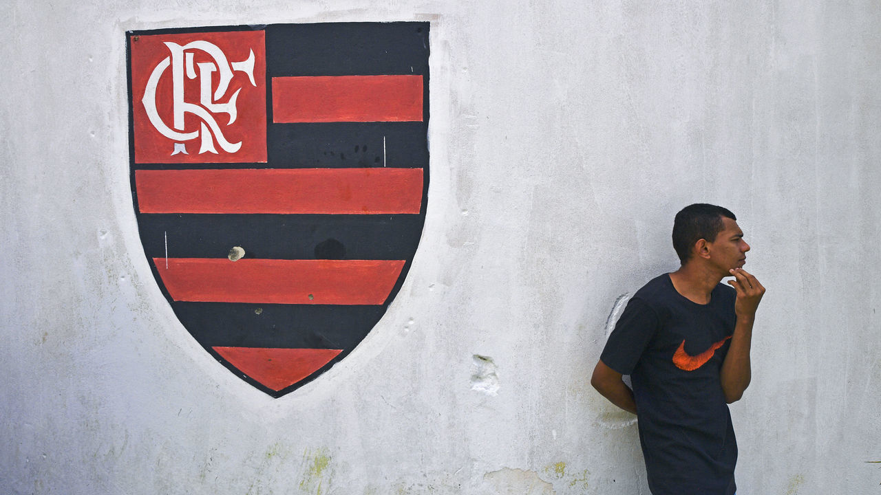 A man stands next to the emblem of Brazilian football club Flamengo painted on a wall outside its training center, after it caught fire in Rio de Janeiro, Brazil on February 8, 2019. - Fire swept through a training facility for Brazil's most popular football club Flamengo Friday, killing at least 10 people, authorities said.