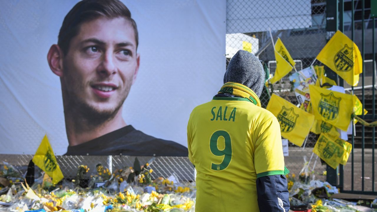 Supporters pay tribute and look at yellow flowers displayed in front of the portrait of Argentinian forward Emiliano Sala at the Beaujoire stadium in Nantes, on February 10, 2019. - FC Nantes football club announced on February 8, 2019 that it will freeze the #9 jersey as a tribute to Cardiff City and former Nantes footballer Emiliano Sala who died in a plane crash in the English Channel on January 21, 2019.