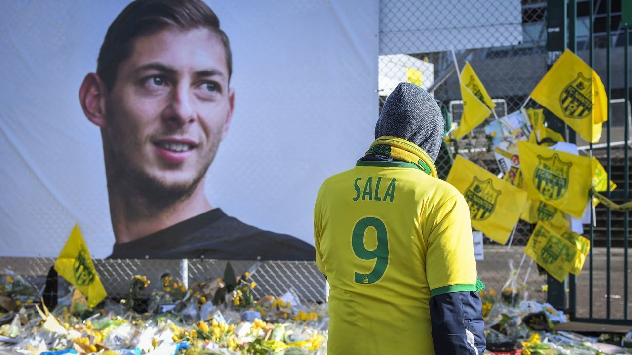 Supporters pay tribute and look at yellow flowers displayed in front of the portrait of Argentinian forward Emiliano Sala at the Beaujoire stadium in Nantes, on February 10, 2019. - FC Nantes football club announced on February 8, 2019 that it will freeze the #9 jersey as a tribute to Cardiff City and former Nantes footballer Emiliano Sala who died in a plane crash in the English Channel on January 21, 2019.