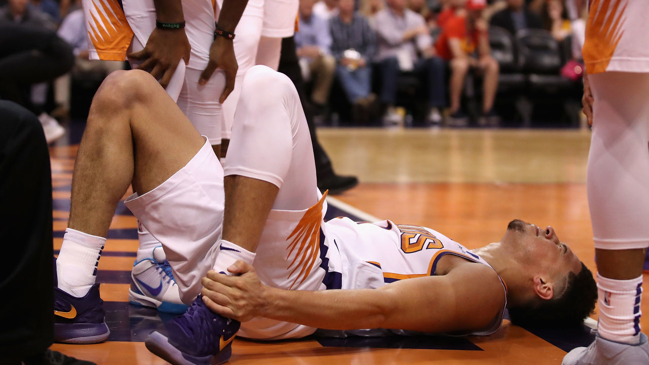 PHOENIX, ARIZONA - APRIL 03: Devin Booker #1 of the Phoenix Suns holds his ankle after an injury during the first half of the NBA game against the Utah Jazz at Talking Stick Resort Arena on April 03, 2019 in Phoenix, Arizona.