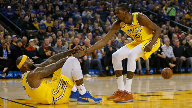 OAKLAND, CA - FEBRUARY 21: DeMarcus Cousins #0 of the Golden State Warriors is helped to his feet by teammate Kevin Durant #35 after drawing an offensive foul against the Sacramento Kings at ORACLE Arena on February 21, 2019 in Oakland, California.