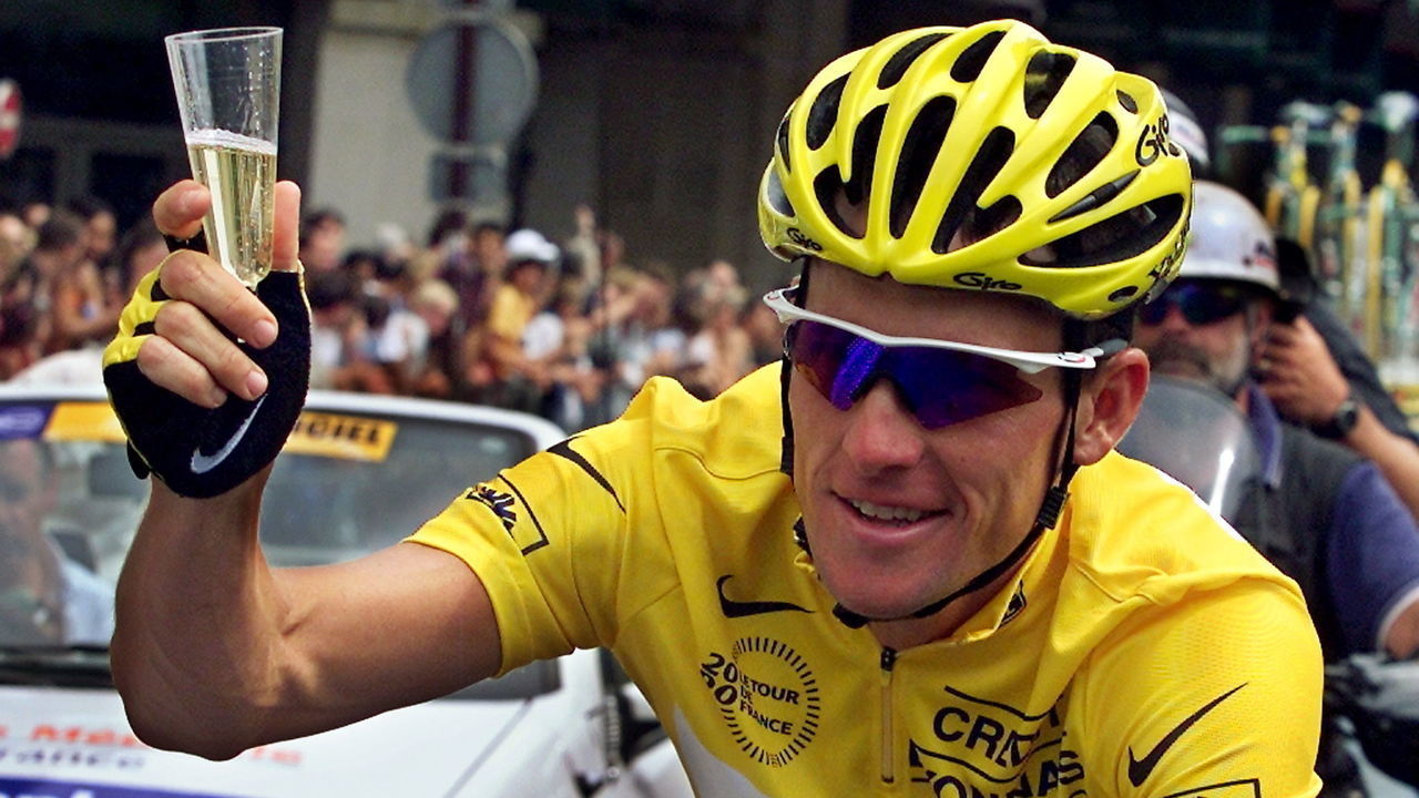 The yellow jersey US Lance Armstrong holds a cup of champagne as he rides during the last stage of the 87th Tour de France in Paris 23 July 2000. AFP PHOTO PATRICK KOVARIK