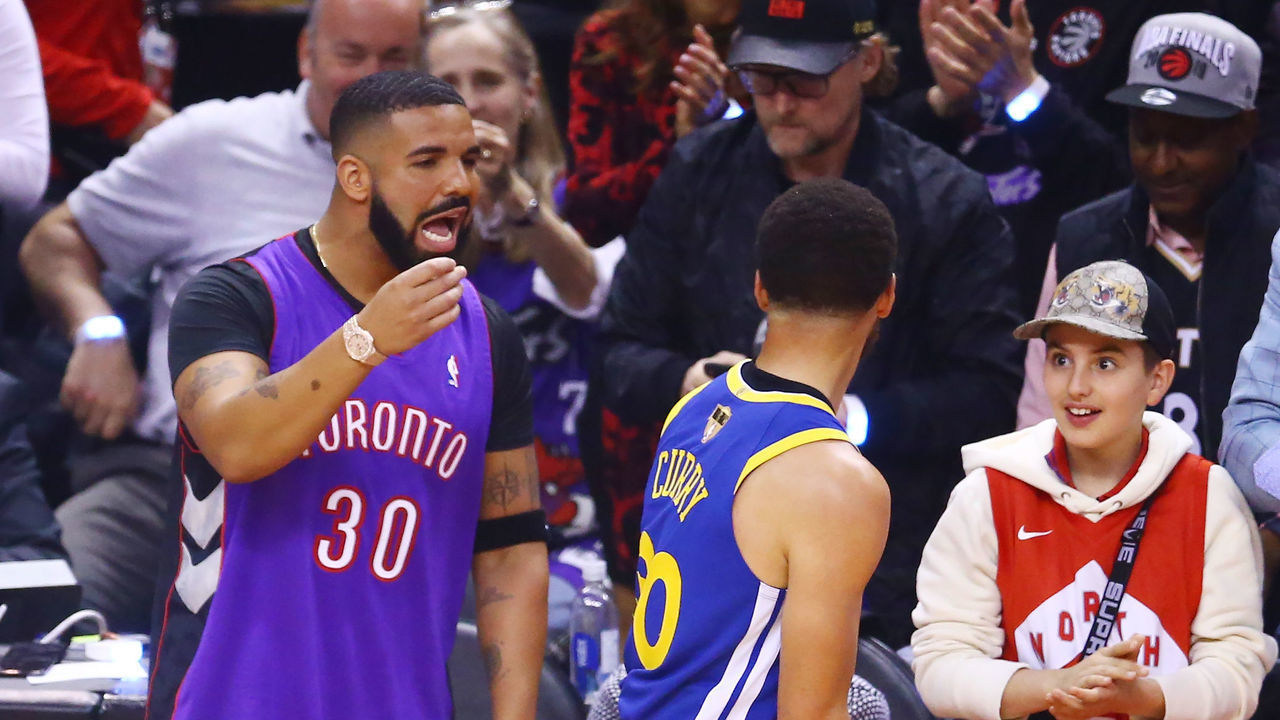 TORONTO, ONTARIO - MAY 30: Rapper Drake and Stephen Curry #30 of the Golden State Warriors exchange words during a timeout in the first quarter during Game One of the 2019 NBA Finals between the Golden State Warriors and the Toronto Raptors at Scotiabank Arena on May 30, 2019 in Toronto, Canada.