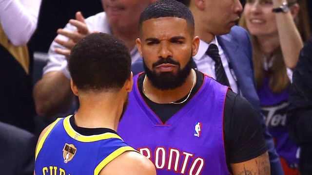 TORONTO, ONTARIO - MAY 30: Rapper Drake and Stephen Curry #30 of the Golden State Warriors exchange words during a timeout in the first quarter during Game One of the 2019 NBA Finals between the Golden State Warriors and the Toronto Raptors at Scotiabank Arena on May 30, 2019 in Toronto, Canada.