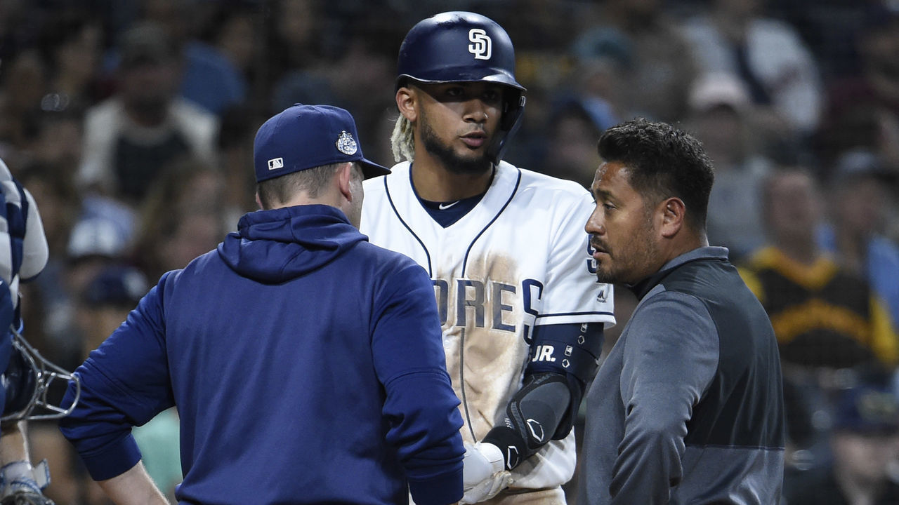 SAN DIEGO, CA - AUGUST 13: Andy Green #14 of the San Diego Padres and a trainer talk with Fernando Tatis Jr. #23 during the sixth inning of a baseball game against the Tampa Bay Rays at Petco Park August 13, 2019 in San Diego, California.