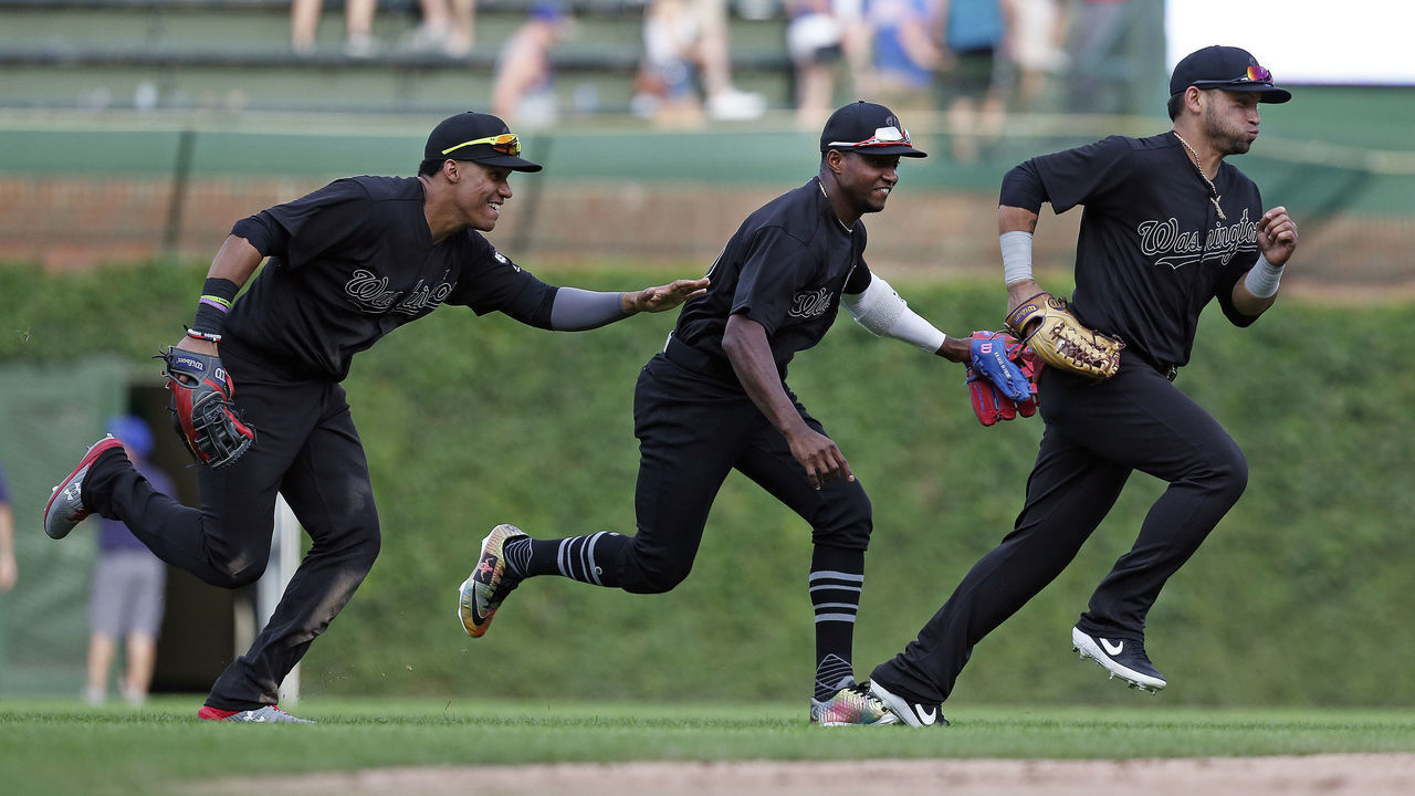 CHICAGO, ILLINOIS - AUGUST 25: (L-R) Juan Soto #22, Victor Robles #16 and Gerardo Parra #88 of the Washington Nationals celebrate at the end of their team's 7-5 win over the Chicago Cubs at Wrigley Field on August 25, 2019 in Chicago, Illinois. Teams are wearing special color schemed uniforms with players choosing nicknames to display for Players' Weekend.