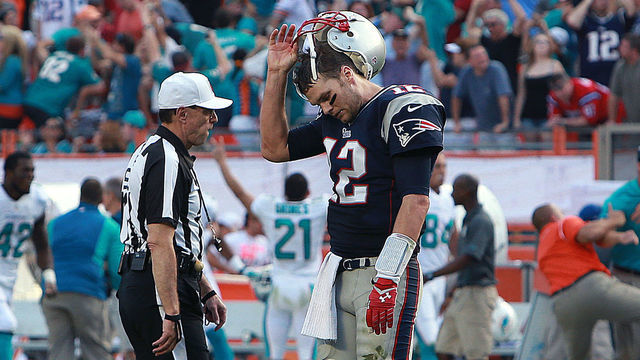 MIAMI GARDENS, FL - DECEMBER 15: As Dolphins players, coaches, and fans (except for one New England fan wearing a Brady jersey) celebrate, Patriots quarterback Tom Brady (#12) walks off the field after throwing an interception in the end zone at the end of the game, wrapping up Miami's 24-20 victory. The New England Patriots visited the Miami Dolphins in a regular season NFL game at Sun Life Stadium.