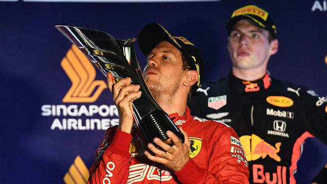 Ferrari's German driver Sebastian Vettel (C) kisses the trophy on the podium after his victory as third-placed Red Bull's Dutch driver Max Verstappen (R) looks on, at the awards ceremony following the Formula One Singapore Grand Prix night race at the Marina Bay Street Circuit in Singapore on September 22, 2019.