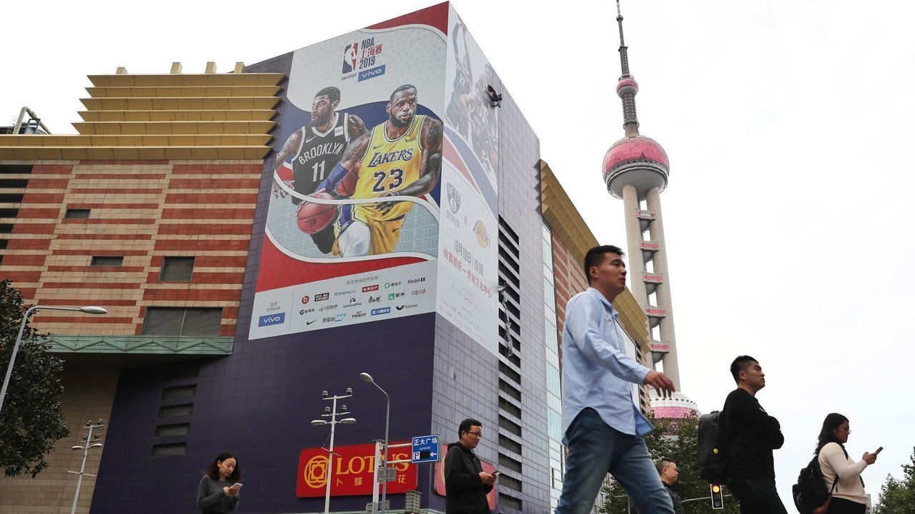 SHANGHAI, CHINA - OCTOBER 09: People walk down a stress as a worker removes a large poster from a building ahead of NBA Shanghai Game 2019 between Brooklyn Nets and Los Angeles Lakers at the Lujiazui Zhengda Plaza on October 9, 2019 in Shanghai, China.