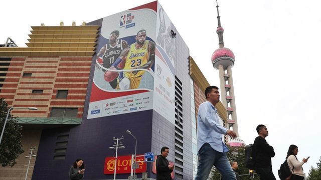 SHANGHAI, CHINA - OCTOBER 09: People walk down a stress as a worker removes a large poster from a building ahead of NBA Shanghai Game 2019 between Brooklyn Nets and Los Angeles Lakers at the Lujiazui Zhengda Plaza on October 9, 2019 in Shanghai, China.
