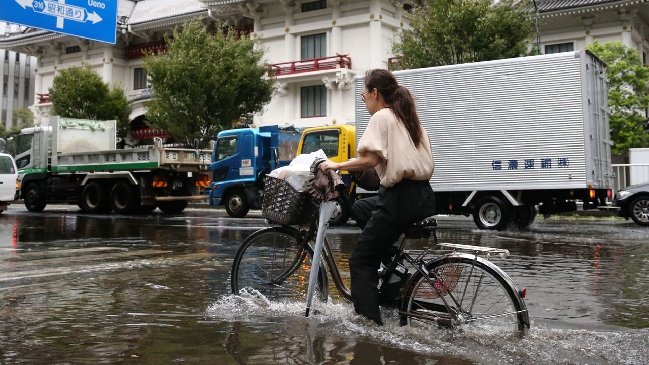 A woman cycles through a flooded area in Tokyo on September 9, 2019. - A powerful typhoon with potentially record winds and rain battered the Tokyo region on September 9, sparking evacuation warnings to tens of thousands, widespread blackouts and transport disruption.