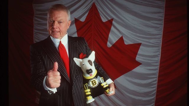 TELE VISION PERSONALITY DON CHERRY POSES IN FRONT OF THE CANADIAN FLAG WITH A BOSTON BRUIN DOG DURING A PHOTO SHOOT.