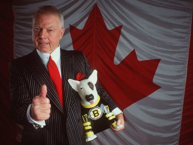 TELE VISION PERSONALITY DON CHERRY POSES IN FRONT OF THE CANADIAN FLAG WITH A BOSTON BRUIN DOG DURING A PHOTO SHOOT.