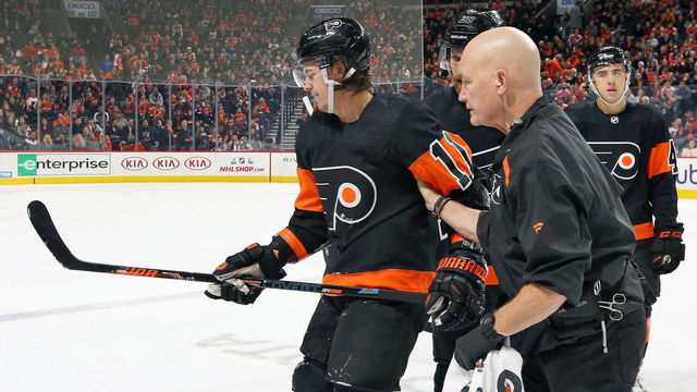 PHILADELPHIA, PA - DECEMBER 07: Travis Konecny #11 of the Philadelphia Flyers is helped off the ice by the teams Director of Sports Medicine Jim McCrossin following a center ice collision with Mark Borowiecki #74 (not pictured) of the Ottawa Senators on December 7, 2019 at the Wells Fargo Center in Philadelphia, Pennsylvania.