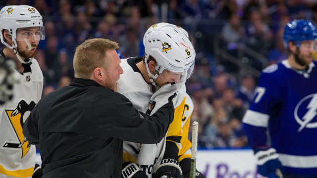TAMPA, FL - FEBRUARY 6: John Marino #6 of the Pittsburgh Penguins is tended to by team Head Athletic Trainer Chris Stewart against the Tampa Bay Lightning during the third period at Amalie Arena on February 6, 2020 in Tampa, Florida.