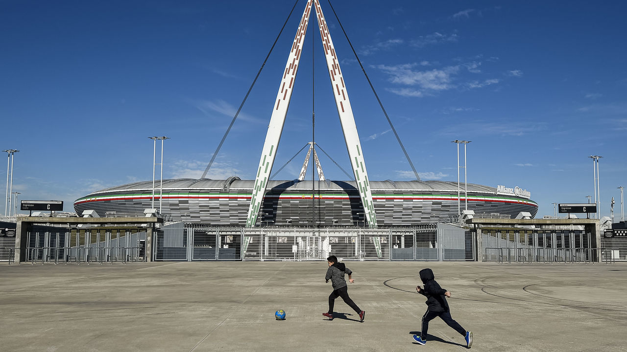 ALLIANZ STADIUM, TURIN, ITALY - 2020/03/04: Two children play with a ball outside desert Allianz Stadium (also known as Juventus Stadium). The Italian Cup semifinal second leg football match between Juventus FC and AC Milan scheduled for Wednesday, March 4 has been postponed indefinitely as part of measures to stop the spread of the coronavirus COVID-19 outbreak in Italy. Media say that Italian government will implement measures to cancel all sporting events for 30 days, although football matches may yet be allowed to take place behind closed doors.