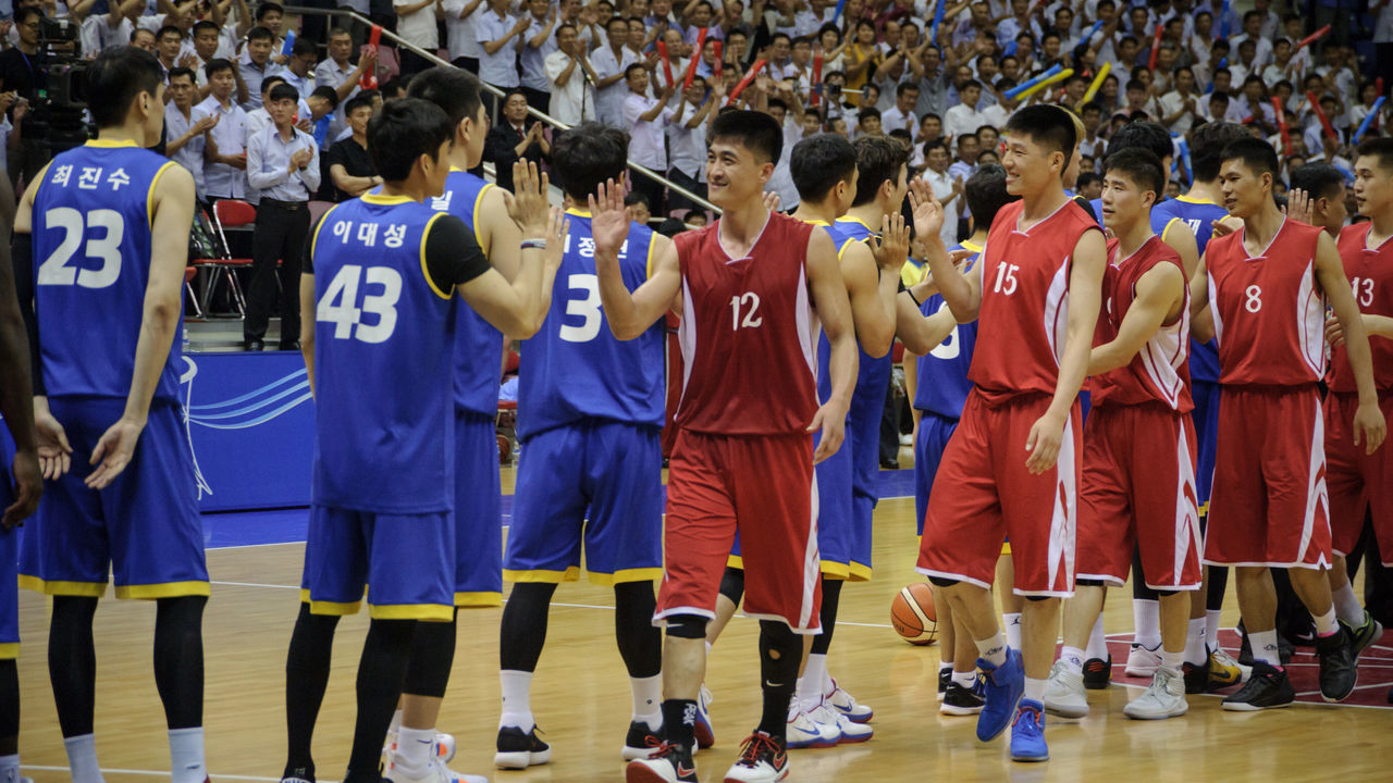 This photo taken on July 5, 2018 shows players from North (red) and South Korea (blue) greeting each other following a friendly men's basketball match at the Ryugyong Chung Ju-Yung Indoor Stadium in Pyongyang. - The North Korean men's team won 82-70. A group of 50 male and female players from the South arrived in the North's capital on July 3 for four rounds of friendlies -- agreed at the inter-Korea summit held in April.