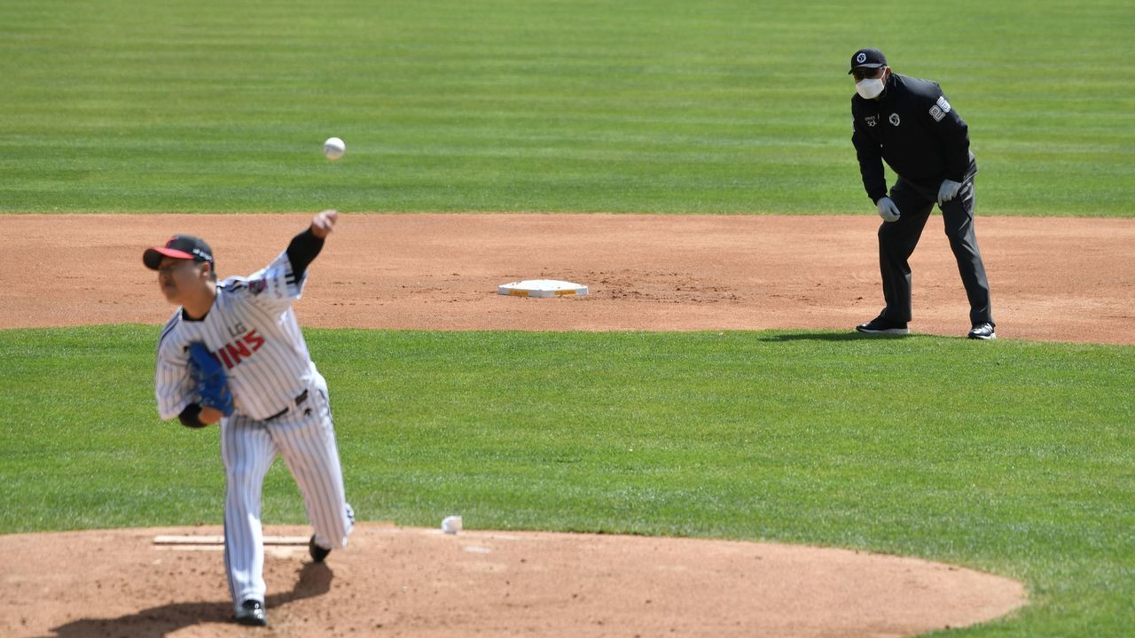 LG Twins pitcher Cha Woo-chan (L) throws a ball as a referee (R) wearing a face mask looks on during a pre-season baseball game between Seoul-based Doosan Bears and LG Twins at Jamsil stadium in Seoul on April 21, 2020. - Professional sport returned to South Korea on April 21 as coronavirus restrictions ease, with the first pitch thrown in a baseball preseason derby in front of empty stands.