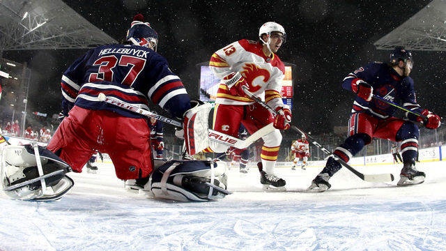 REGINA, SASKATCHEWAN - OCTOBER 26: Goaltender Connor Hellebuyck #37 of the Winnipeg Jets defends the net against Johnny Gaudreau #13 of the Calgary Flames during the 2019 Tim Hortons NHL Heritage Classic at Mosaic Stadium on October 26, 2019 in Regina, Canada.