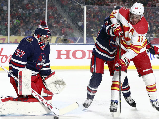 REGINA, SASKATCHEWAN - OCTOBER 26: Goaltender Connor Hellebuyck #37 of the Winnipeg Jets makes a save on a scoring attempt by Matthew Tkachuk #19 of the Calgary Flames in the first period of the 2019 Tim Hortons NHL Heritage Classic between the Calgary Flames and the Winnipeg Jets at Mosaic Stadium on October 26, 2019 in Regina, Canada.