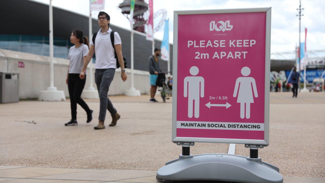People walk by a sign reminding of the social distancing rules as a precaution against COVID-19 in the Olympic Park outside The London Stadium, in east London on June 20, 2020 before kick off of the English Premier League football match between West Ham United and Wolverhampton Wanderers.