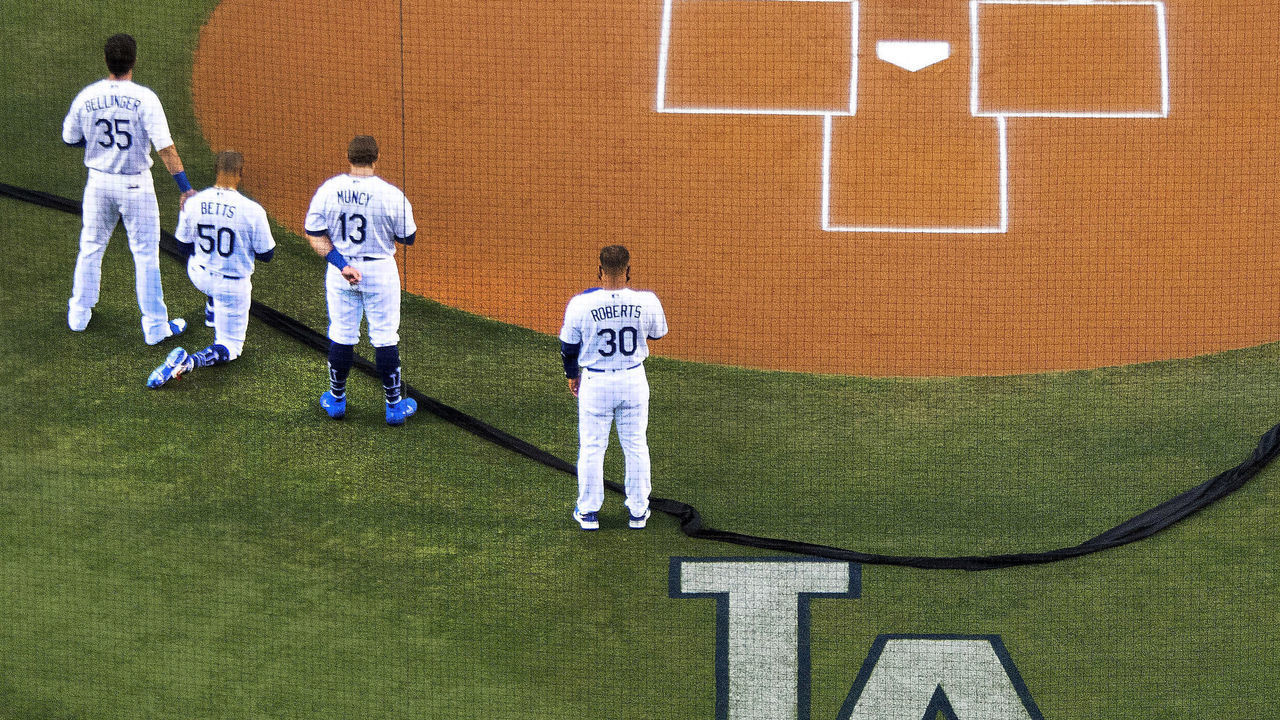 LOS ANGELES, CA - JULY 23: Cody Bellinger #35 of the Los Angeles Dodgers places his hand on the shoulder of teammate Mookie Betts #50 who kneels as Max Muncy #13 of the Los Angeles Dodgers and manager Dave Roberts #30 stand during the National Anthem rior to a MLB baseball game on Opening Day at Dodger Stadium in Los Angeles on Thursday, July 23, 2020.