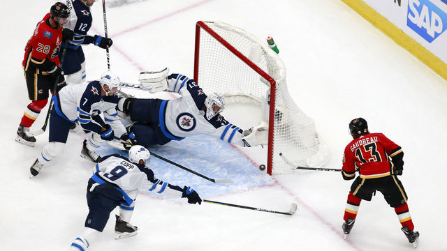 EDMONTON, ALBERTA - AUGUST 01: Johnny Gaudreau #13 of the Calgary Flames scores a goal as Connor Hellebuyck #37 of the Winnipeg Jets dives to defend in Game One of the Western Conference Qualification Round prior to the 2020 NHL Stanley Cup Playoffs at Rogers Place on August 01, 2020 in Edmonton, Alberta.