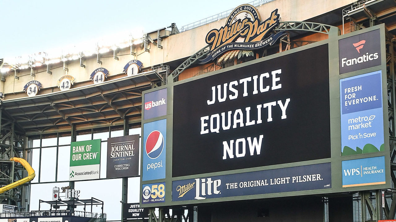 MILWAUKEE, WI - AUGUST 26: The words "Justice Equality Now" are displayed on the jumbotron behind two members of the Milwaukee Brewers as they play catch in Black Lives Matter t-shirts at Miller Park after a Major League Baseball game between the Milwaukee Brewers and Cincinnati Reds was postponed on August 26, 2020 as a response by the players of the Milwaukee Brewers to the shooting of Jacob Blake, a 29-year-old Black man by Kenosha, Wisconsin, police on August 19, 2020 .
