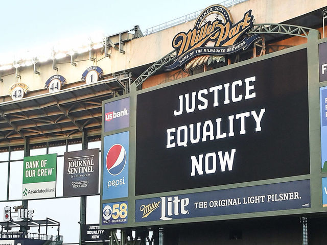 MILWAUKEE, WI - AUGUST 26: The words "Justice Equality Now" are displayed on the jumbotron behind two members of the Milwaukee Brewers as they play catch in Black Lives Matter t-shirts at Miller Park after a Major League Baseball game between the Milwaukee Brewers and Cincinnati Reds was postponed on August 26, 2020 as a response by the players of the Milwaukee Brewers to the shooting of Jacob Blake, a 29-year-old Black man by Kenosha, Wisconsin, police on August 19, 2020 .