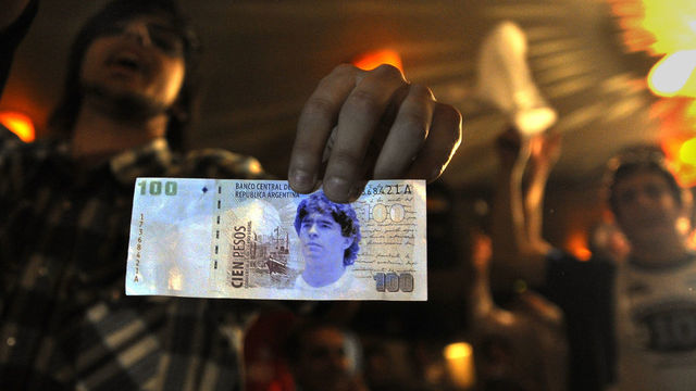 A member of the Maradonian Church The hand of God, a religion dedicated to the Argentina's greatest ever soccer player Diego Maradona, shows a fake one hundred pesos bill during their Christmas celebration the night before Maradona's 48th birthday in Buenos Aires on October 29, 2008. A congregation of hundreds gathered at the Hand of God chapel to pay due respect at midnight on the occasion of the new Argentina's national soccer team coach birthday. AFP PHOTO / DANIEL GARCIA