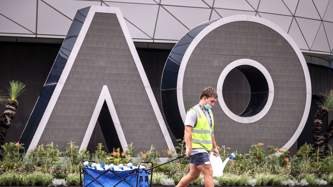 A worker wearing a face mask pulls next to a sign promoting the Australian Open in Melbourne on January 30, 2021. - The world's top tennis stars emerge from two weeks stuck in their hotel rooms due to quarantine imposed upon their arrival ahead of the Australian Open tennis tournament starting on February 8.