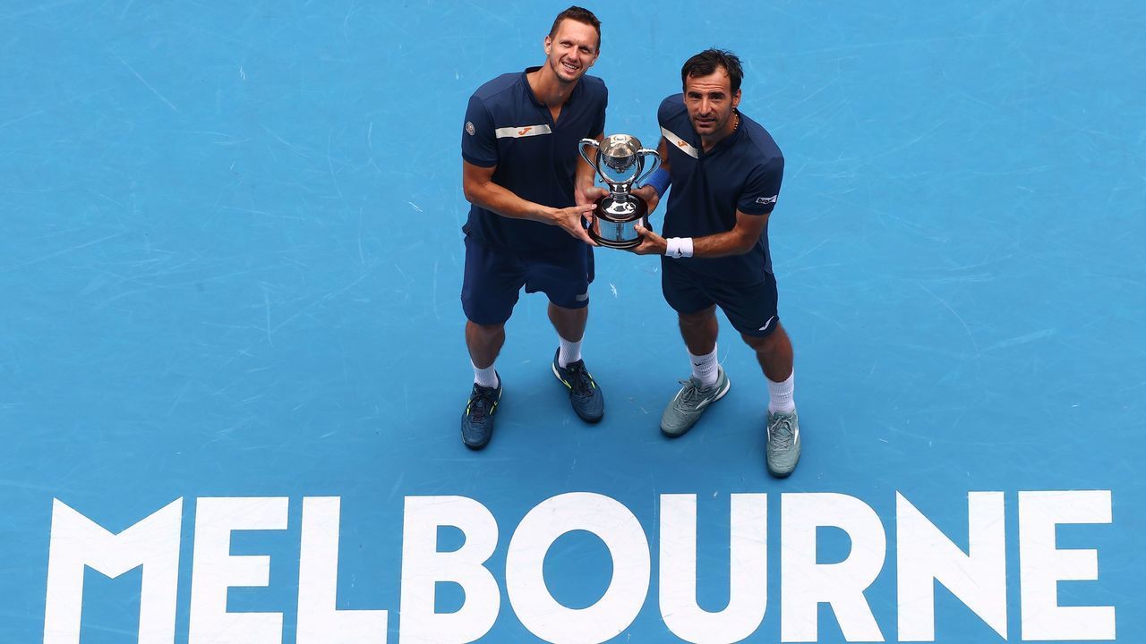 Croatia's Ivan Dodig (R) holds the championship trophy with partner Slovakia's Filip Polasek after winning their men's doubles final match against Rajeev Ram of the US and partner Britain's Joe Salisbury on day fourteen of the Australian Open tennis tournament in Melbourne on February 21, 2021.